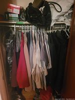 Closet full of men's and women's clothing on hangers, showing mostly shirts and dresses in various colors including cream, pink, and black colors
