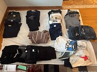 Photo showing several dark sweaters, polo shirts, t-shirts, and folded jeans laid out on floor cloth