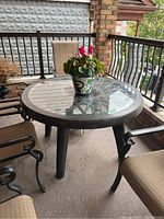 Round patio table on porch with polymer resin frame and removable glass top with lattice design underneath. Visible surface wear on glass.
