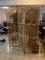 Front and angled views of a three-panel wicker privacy screen placed on a tiled floor indoors, showing circular woven wicker design on each panel.