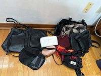 Multiple purses, fanny packs, and zippered pouches arranged on floor showcasing variety and condition.