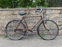 Side view of vintage Raleigh Sports cruiser bicycle with brown frame, black Brooks saddle, and rear rack.