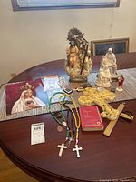 Image showing entire lot arranged on a table: Bible, ceramic figurines, rosaries, photo of Virgin Mary, devotional cards, and yellow fabric item.