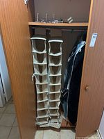 Two beige cloth hanging shoe rack organizers hanging inside a wooden closet. Each rack has multiple vertical compartments and visible metal and plastic hooks at the top for hanging.