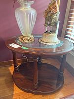 Side table in brown wood with rounded legs and glass top holding vase and figurine, showing overall shape and design.