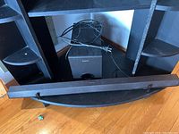 Overall view of Sony sound bar and subwoofer placed under black shelving unit with wires visible