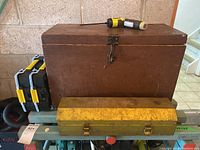 Image shows three toolboxes: a large brown wooden toolbox with latch, a yellow metal toolbox, and a black and yellow plastic toolbox with clasps.