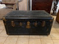 Front view of antique steamer wardrobe trunk showing metal latches, lock area, and worn black covering with studs.