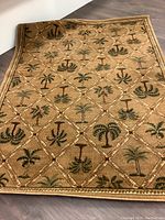 Full view of a beige-tan area rug with diamond pattern and palm tree motifs inside each diamond, showing the overall design and colors.