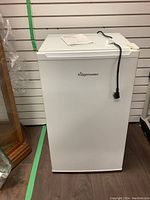 White Fridgemaster bar fridge closed with power cord on top and instruction manual.