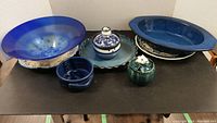Full assortment of bowls and serving dishes in blue ceramic, glass, and pottery on black surface