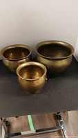 Three matching brass pots shown together with hammered texture and aged patina
