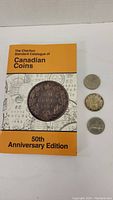 Photo showing Charlton Standard Catalogue of Canadian Coins 50th Anniversary Edition book with three Canadian silver dollar coins.