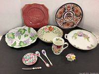 Full view of the china serveware lot showing plates, bowls, mugs, spoons, and decorative piece all arranged on surface.