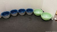 Overview of 4 blue and white Corelle bowls and 2 vintage green Fire King bowls on a black surface against a cardboard background.