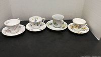 Front view of all 4 cups and saucers set in a row on black surface with white background