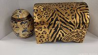 Gold and black animal print chest-style box and painted egg-shaped decor item placed side by side