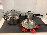 Overview of all cookware items: large steam pot with lid, two saucepans with lids, frying pan on black surface.