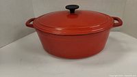 Front and side view of red oval casserole pot with lid and handles on white background