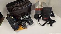 Photo showing Pentax ME Super camera with lens attached, additional Pentax lens, leather camera bag, flash unit and cleaning paper.