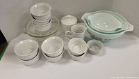 Full lot of vintage kitchenware displayed with mixing bowls, ramekins, covered sugar bowl, creamer and clear glass bowl with lid.