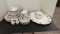 Full set displayed at front showing stacked plates, cups, saucers, shakers, platter and gravy boat.