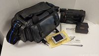 Black Sony Video 8 Handycam camcorder with case, manual and small boxes laid out on surface.