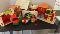 Full set of vintage Fisher Price Play Family Village buildings and toys laid out on a table including multiple buildings and activity blocks.
