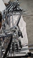 Pile of metal chrome clothing rack frames with caster wheels showing adjustable height holes and locking wheels.