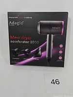 Front of the box showing Adagio Accelerator 2000 blow dryer image and included attachments (styling nozzle, large nozzle, diffuser).