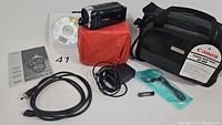 Canon Vixia HF R30 camcorder and included accessories arranged showing cables, software, charger, and carrying bag with original Canon sticker