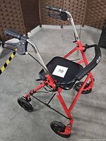 Front angle view showing seat, removable back support, and handle brake controls on red aluminum frame with black wheels.