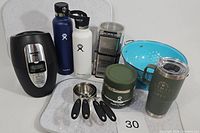 Photo showing entire lot: wine chiller, two Hydroflask bottles, manual coffee grinder, green Hydroflask food jar, melamine platters, measuring cups, blue colander, and Yeti tumbler.