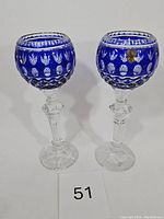 Pair of tall blue and clear cut crystal chalices standing upright on a white surface, showing front and side views.