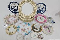 Overview photo showing a collection of plates including 6 ornate Limoges plates, 3 Bavarian-style blue and white plates, floral themed plates, and one teacup with saucer.