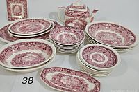Across view of the entire set showing teapot, large and small platters, plates and bowls all in red transferware pattern on white background.