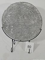 Full view of round 18-inch diameter fused metal display art piece by Michael Aram positioned on black metal stand.