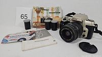 Photo shows the Nikon N60 camera body with lens, 2 rolls of film, several manuals including instruction manual and promotional booklets, and a lens cap.