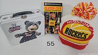 Photo shows the lunchbox with Clutch mascot image on one side, the VHS tape titled 'Clutch City,' and a Houston Rockets knit beanie with pom-pom in Rockets colors arranged together.
