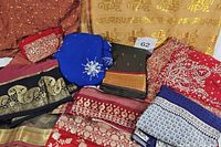 View of assembled sari fabrics showing various colors including red, blue, gold, navy, and beige, with intricate embroidery and beadwork.