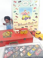 Full view of the lot including the vintage Erector Set red metal box, Kiddie Car Classics poster, black doll, a yellow toy truck, cast iron horse-drawn cart, and NASCAR model cars in a display case.