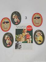 Photo displaying five vintage Coca Cola metal trays featuring various women in 1930s attire and a 1938 Coca Cola print advertisement.