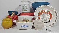 Full view of vintage dishware lot showing yellow Le Creuset honey pot with lid, Longaberger sugarbowl, two Corning Ware dishes, strawberry pie dish with recipe, floral pitcher, owl bowl, and blue bowl.