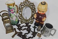 Full lot with various vintage oddities including brass filigree mirror frame, grape pitcher, Kewpie bank, lantern, pewter mug, bottle opener, drawer pulls, hex key, ashtray and taper tipper.