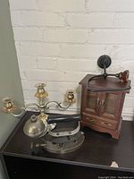 Photo of four items: silver-toned candelabra, heavy iron, wooden jewelry box with small door and attached amber colored toilet paper holder.
