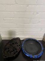 Wood carved grapevine tray and Crown Ducal Ware ceramic bowl showing front views on black surface against white brick wall