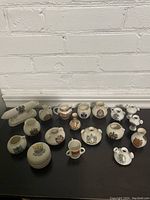 Photo showing 18 miniature vases and urns arranged on a black surface against a white brick wall, highlighting different shapes, sizes, and decorative crests.