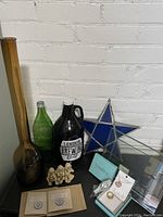 Photo showing mixed lot items: brown and green glass bottles, dark brown handled bottle, blue stained glass star tealight holder, small beige carved figurine, and heavy glass picture frame.