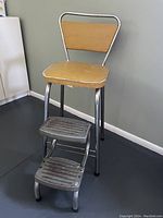 Side view of the retro kitchen stool showing chrome frame, yellow vinyl upholstered seat and foldable metal step ladder with two steps.
