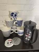 Six Royal Doulton mugs stacked with blue and white Pacific patterns including dots, stripes, and splatter designs, arranged next to a Bodum French Press coffee maker with lid and plunger disassembled and displayed.
